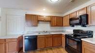 This single-story, 3-bedroom, 2-bathroom home offers a practical and comfortable layout across a thoughtfully organized floor plan. The kitchen is a functional highlight, featuring warm honey-toned wood cabinetry, light granite-style countertops, and a full suite of black appliances including a range, dishwasher, refrigerator, and over-the-range microwave. The L-shaped counter configuration maximizes workspace, while durable hardwood-style flooring ties the kitchen and main living areas together seamlessly. The open living area is bright and welcoming, with natural light filtering through windows and a ceiling fan overhead. Three bedrooms are each finished with plush neutral carpeting and ceiling fans, offering a comfortable retreat. The spacious primary bedroom provides a generous footprint, while the additional bedrooms share a similar layout and feel. Three closets throughout the home ensure ample storage. The two bathrooms are clean and functional — one features a full tub/shower combo with white surrounds and chrome fixtures, while the second includes a wood-toned vanity with a granite-style countertop and hardwood-style flooring. A connecting hallway ties the layout together efficiently, completing this well-appointed home.