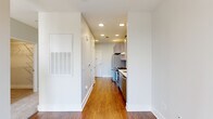 This well-designed one-bedroom, one-bathroom unit offers a thoughtfully organized layout across a single floor, making efficient use of every square foot. A central hallway connects the main living areas, finished with warm hardwood-style flooring and crisp white walls illuminated by recessed lighting throughout.

The kitchen is outfitted with stainless steel appliances, including a gas range with a sleek overhead range hood and a full-size refrigerator. Light gray cabinetry lines the walls, complemented by a classic subway tile backsplash and light countertops, creating a clean, modern aesthetic. The entry door opens directly into this space, offering a practical flow.

The bedroom is a comfortable, carpeted retreat featuring large windows that allow natural light to fill the room. A ceiling fan adds functional comfort, and an adjacent walk-in closet with built-in shelving and hanging rods provides ample storage.

The bathroom is finished with light-toned tile flooring and features a full soaking tub with a tiled surround in a classic subway pattern. Brushed nickel grab bars and a curved shower rod add both style and practicality to the space.

Overall, this unit presents a clean, contemporary design with durable finishes and a neutral palette that offers a versatile and livable environment.