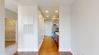 This well-designed one-bedroom, one-bathroom unit offers a thoughtfully organized layout across a single floor, making efficient use of every square foot. A central hallway connects the main living areas, finished with warm hardwood-style flooring and crisp white walls illuminated by recessed lighting throughout.

The kitchen is outfitted with stainless steel appliances, including a gas range with a sleek overhead range hood and a full-size refrigerator. Light gray cabinetry lines the walls, complemented by a classic subway tile backsplash and light countertops, creating a clean, modern aesthetic. The entry door opens directly into this space, offering a practical flow.

The bedroom is a comfortable, carpeted retreat featuring large windows that allow natural light to fill the room. A ceiling fan adds functional comfort, and an adjacent walk-in closet with built-in shelving and hanging rods provides ample storage.

The bathroom is finished with light-toned tile flooring and features a full soaking tub with a tiled surround in a classic subway pattern. Brushed nickel grab bars and a curved shower rod add both style and practicality to the space.

Overall, this unit presents a clean, contemporary design with durable finishes and a neutral palette that offers a versatile and livable environment.