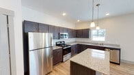 Located in Hudsonville, Michigan, this single-floor residence offers a thoughtfully designed layout with modern finishes throughout. The open-concept kitchen is a standout feature, showcasing rich dark-stained cabinetry, granite countertops, a central island, stainless steel appliances including a refrigerator, electric range, and built-in microwave, all illuminated by stylish pendant lighting. Light hardwood flooring runs throughout the main living areas, contributing to a warm and cohesive aesthetic. The spacious living area is filled with natural light from multiple windows and a sliding glass door that opens to the outdoors, creating a bright and airy atmosphere. The bedrooms are carpeted for comfort, each featuring windows that bring in natural light. The primary bedroom includes direct access to an en-suite bathroom equipped with a walk-in shower, dark cabinetry, and granite countertops. A second full bathroom offers a tub-shower combination and matching granite vanity. Neutral wall tones and recessed lighting throughout lend the space a clean, contemporary feel, while the overall layout provides a practical and comfortable living environment well-suited to everyday life in Hudsonville.