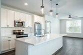 Located at 6231 Williamsburg Way in De Forest, Wisconsin, this well-appointed single-floor home offers 2 bedrooms and 4 bathrooms within a thoughtfully designed layout. The heart of the home is a bright, open-concept space that seamlessly integrates the kitchen, dining, and living areas. The kitchen is a standout feature, anchored by a large center island with a white quartz countertop, undermount sink, and stylish pendant lighting overhead. White shaker cabinetry, a subway tile backsplash, and stainless steel appliances complete the modern aesthetic. Wood-look flooring flows throughout the main living spaces, complemented by abundant natural light from multiple windows. The bedrooms offer plush carpeting, ceiling fans, and generous windows with exterior views. Five closets provide ample storage throughout. The bathrooms are finished with white cabinetry, quartz countertops, framed mirrors, and dark hardware accents, maintaining a consistent, clean design language. A dedicated entrance, patio, and open hallway with multiple closet access points add to the home's functionality. Dark door trim and black hardware details throughout add a modern contrast to the bright, neutral palette, creating a cohesive and contemporary living environment.