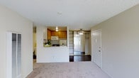 Located at 5550 Genessee in San Diego, this single-floor residence offers a practical and well-organized layout designed to maximize every inch of available space. The living area features light-toned carpeting that creates a warm, neutral foundation throughout, while a textured ceiling adds subtle architectural character overhead. A pass-through kitchen with warm wood cabinetry, a built-in microwave, and a gas range connects seamlessly to the living space, making it ideal for everyday convenience and casual entertaining. The kitchen's half-wall design promotes an open, airy feel while maintaining a defined cooking zone. Adjacent to the living area, a built-in shelving unit with multiple tiers provides ample storage and display space, complemented by a ceiling fan light fixture that enhances both functionality and ambiance. The front entry is marked by a solid door with a polished knob, offering a clean and secure transition from the exterior. Dark hardwood flooring in the entryway and shelving alcove contrasts neatly with the carpeted living space, adding visual depth and a touch of elegance. Overall, the residence presents a straightforward, functional design well-suited to San Diego's relaxed lifestyle.