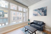 Located on Bromfield Street in the heart of downtown Boston, this one-bedroom, one-bathroom unit offers a thoughtfully designed layout that maximizes every inch of its compact footprint. The space is defined by a striking slatted ceiling detail that runs through the kitchen and living areas, adding architectural character and visual depth throughout.

The galley-style kitchen lines one wall with white shaker cabinetry, subway tile backsplash, stainless steel appliances including a range, over-the-range microwave, and refrigerator, all set against light hardwood flooring that flows continuously through the unit. A corridor leads to the bright living area, where oversized, multi-pane windows frame direct views of Bromfield Street and the surrounding historic Boston streetscape, flooding the room with natural light. A wall-mounted mini-split unit provides climate control.

The bedroom continues the theme of generous natural light, featuring the same large street-facing windows and light hardwood floors, along with ample closet storage — three closets in total across the unit. The bathroom is finished with grey marble-style tile flooring, a navy vanity with gold hardware, a frameless glass shower enclosure, and a clean, modern aesthetic. The overall ambiance is contemporary and bright, well-suited for urban living in one of Boston's most central neighborhoods.