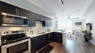 Located at 355 N Rosalind Ave in the heart of Orlando, FL, this contemporary single-floor residence delivers a clean, modern aesthetic throughout. The kitchen is a standout feature, showcasing dark cabinetry with brushed chrome hardware, crisp white quartz countertops, a subway tile backsplash, and a full suite of stainless steel appliances including a range, built-in microwave, refrigerator, and dishwasher. A peninsula counter connects the kitchen to the living area, creating an open, flowing layout ideal for entertaining. The living space is bright and airy, benefiting from a large window that invites abundant natural light, complemented by wood-style flooring that runs throughout the main areas. The bedroom offers a comfortable, carpeted retreat with generous window coverage, allowing for natural light while maintaining privacy. Closet space is well-organized with built-in shelving for efficient storage. The bathroom is finished with wood-look tile flooring, a dark vanity with white countertop, and a glass-enclosed walk-in shower with tiled surround. Neutral wall tones and a consistent modern design language tie every room together, creating a cohesive and polished living environment in one of Orlando's most accessible urban locations.