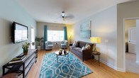 This thoughtfully designed single-floor residence offers a comfortable and stylish living experience across a range of well-defined spaces. The open living room is anchored by warm hardwood-style flooring, a ceiling fan, and large windows dressed with vibrant teal curtains that fill the room with natural light. A wall-mounted TV and rustic industrial media console add functional character to the space, which also features direct access to an exterior door. The kitchen is outfitted with rich dark cabinetry, granite-style countertops, stainless steel appliances including a range and microwave, and glass-front upper cabinets — combining both style and practicality. The residence includes multiple bedrooms, each carpeted for comfort and featuring ample natural light. The primary bedroom boasts a walk-in closet, while additional bedrooms offer generous space and storage. Two bathrooms mirror the kitchen's design aesthetic, featuring dark wood vanities, granite countertops, and framed mirrors. One bathroom includes a tub-shower combination. A dedicated in-unit laundry room with a full-size washer and dryer adds everyday convenience. Throughout, the home maintains a cohesive palette of soft blues, warm neutrals, and natural wood tones, creating an inviting and harmonious atmosphere.