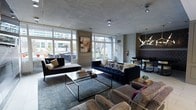 This elegantly designed single-floor space exudes a modern, upscale ambiance defined by thoughtful interior choices and a refined aesthetic. The main lounge area is a standout, showcasing a rich navy blue tufted sofa as its centerpiece, complemented by plush accent chairs in warm, patterned upholstery. A sleek, low-profile coffee table with an open metal frame anchors the seating arrangement, which rests on a sophisticated area rug that adds texture and depth to the room. Large floor-to-ceiling windows wrap the space in generous natural light while framing views of the surrounding urban landscape, creating a seamless connection between the interior and the cityscape beyond. The ceiling features a smooth, polished concrete finish that lends an industrial-chic character, offset by carefully placed modern light fixtures, including a striking geometric chandelier that adds a sculptural element to the dining or bar area in the background. Wall paneling with curated artwork contributes to the gallery-like quality of the space. The overall atmosphere is cosmopolitan and inviting, blending contemporary design with warm, layered furnishings to create a space that is both visually dynamic and functionally comfortable.