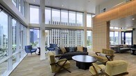 This single-floor lounge space is defined by its dramatic floor-to-ceiling glass walls, which flood the interior with abundant natural light and frame expansive views of the surrounding urban skyline. The double-height ceilings amplify the sense of openness, giving the space an airy, grand quality rarely found in communal settings.

The seating area is thoughtfully arranged around a sleek, dark circular coffee table, anchored by a charcoal sofa adorned with accent pillows in muted tones. Complementing the sofa are olive-green upholstered chairs with wooden X-frame bases, adding a mid-century modern touch, alongside a pair of navy blue accent chairs positioned closer to the windows—ideal for taking in the city views.

A warm wood-paneled accent wall provides textural contrast against the cool, glass-dominated perimeter, balancing the modern aesthetic with natural warmth. Light wood-toned flooring runs throughout, further enhancing the bright, welcoming atmosphere. Structural white columns punctuate the space, reinforcing its architectural character. Overall, the space conveys a polished, contemporary ambiance suited for relaxed gatherings or quiet reflection.