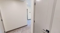 This contemporary 2-bedroom, 2-bathroom unit is located on MacLeod Trail South in Calgary, AB, offering a well-designed single-floor layout with modern finishes throughout. The kitchen serves as the centerpiece of the space, boasting a large waterfall-edge island with an undermount sink, warm wood-toned upper cabinetry paired with sleek grey lower cabinets, a white tile backsplash, and stainless steel appliances. Recessed lighting and large black-framed windows flood the open area with natural light and provide views of the surrounding urban streetscape. The two bedrooms feature light-toned tile-style flooring, clean white walls, and black-framed windows with roller blinds. The primary bedroom offers a generous footprint with direct access to the hallway. The two bathrooms are distinctly designed: one features a glass-enclosed walk-in shower with large marble-effect tiles, grey cabinetry with under-cabinet accent lighting, and matte black fixtures; the other includes a full soaker tub with tiled surround, a floating vanity, and warm-toned floor tiles. A connecting hallway with light grey flooring ties the layout together efficiently, while the consistent use of matte black hardware and neutral tones gives the entire unit a cohesive, contemporary aesthetic.