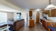This compact yet efficiently designed single-floor residence offers a thoughtful layout across one bedroom and one bathroom. The open-concept living and dining area forms the heart of the space, finished with durable wood-style flooring that runs throughout the main living areas. The living room is bright and inviting, featuring large sliding glass doors with vertical blinds that allow generous natural light and provide views of the surrounding greenery. The dining area, positioned near the entry, includes a pendant light fixture and a full-wall mirror that visually expands the room. Adjacent to the dining space, the galley-style kitchen is practical and well-equipped, featuring warm wood cabinetry, light countertops, and a full suite of appliances including a refrigerator, electric range, and over-the-range microwave. A closeted pantry provides additional storage. The bedroom is a quiet retreat, carpeted for comfort and featuring a window with outdoor views. The full bathroom is cleanly appointed with a shower-tub combination, a single vanity with a wide mirror, and wood-toned cabinetry. Neutral wall tones and consistent finishes throughout give the space a cohesive, move-in-ready appeal.
