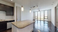 This single-floor residence showcases a thoughtfully designed open-concept layout that seamlessly connects the kitchen, dining, and living areas. Rich, dark hardwood floors run throughout the main living spaces, lending a sleek and contemporary aesthetic. The kitchen is a standout feature, equipped with dark espresso cabinetry, stainless steel appliances, a classic white penny-tile backsplash, and granite countertops that extend across both the perimeter surfaces and a central island. Pendant lighting and a track light system illuminate the space with style.

The living area benefits from an abundance of natural light, courtesy of expansive floor-to-ceiling windows dressed with horizontal blinds. A ceiling fan adds comfort to the bright, airy room. The primary bedroom mirrors this openness with its own set of large windows and ceiling fan, continuing the dark hardwood flooring.

A secondary bedroom offers plush carpeting, a ceiling fan, and a well-sized window with outdoor views. The bathroom is finished with warm travertine-style tile flooring, dark vanity cabinetry, dual granite-topped sinks, a large framed mirror, and a tiled soaking tub and shower combination. Together, these elements create a cohesive, modern living environment with refined finishes throughout.