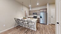 Located in Box Elder, South Dakota, this single-floor unit offers a thoughtfully designed layout that balances modern aesthetics with practical functionality. The open-concept living area is bright and welcoming, featuring wood-style flooring, recessed lighting, and exposed ductwork that lends an industrial character to the space. A large sliding glass door floods the room with natural light and provides outdoor access, while the neutral color palette creates a calm, cohesive atmosphere throughout.

The kitchen is a standout feature, equipped with taupe cabinetry, stainless steel appliances, and a generous island topped with white countertops. Pendant lighting above the island enhances both function and style, and bar seating makes it an ideal spot for casual dining or entertaining.

The bedroom is comfortably sized with plush carpeting, elevated ceilings, and a window fitted with blinds for privacy and light control. It connects directly to a walk-in closet and a full bathroom, which includes a tub-shower combination, wood-style flooring, and clean, contemporary fixtures with matte black hardware accents.

Completing the unit is a dedicated laundry area with a full-size washer and dryer, adding a layer of everyday convenience. The overall design is modern, functional, and well-appointed.