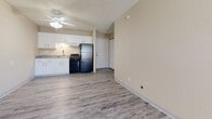 This one-bedroom, one-bathroom apartment offers a practical and well-organized layout across a single floor. The open-concept living and kitchen area creates a cohesive, functional space finished with durable wood-look plank flooring throughout. A ceiling fan with integrated lighting serves the living area, which also includes a wall-mounted air conditioning unit and a baseboard heater, providing year-round climate control. Neutral warm-beige walls complement the light flooring, lending the space a clean, understated aesthetic. A textured ceiling is consistent throughout the unit.

The kitchen is positioned along one wall and features white shaker-style cabinetry with granite-look countertops, a stainless steel sink, an under-cabinet range hood, and black appliances including a gas range and a full-size refrigerator. A closet adjacent to the kitchen provides additional storage near the entryway.

The bedroom is carpeted for comfort and includes a reach-in closet with wire shelving and hanging rods, offering organized storage. The bathroom features a full-size tub and shower combination with a clean white surround and chrome fixtures. The overall design is straightforward and functional, making efficient use of the available space.