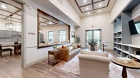 This thoughtfully designed single-floor community space offers a warm, upscale atmosphere through a cohesive modern farmhouse aesthetic. The main lounge area impresses with soaring ceilings accented by elegant coffered woodwork, recessed lighting, and large windows that flood the space with natural light. A generously sized decorative mirror, rich leather seating, and a soft area rug create an inviting and polished gathering area with views to an outdoor patio beyond.

The open kitchen and dining area is a standout feature, showcasing custom gray cabinetry, a subway tile backsplash, stainless steel appliances, and a large farmhouse dining table beneath dramatic black lantern pendant lights. Bar-height seating along a stone-topped counter provides an additional casual dining option, while oversized windows maintain a seamless connection to the outdoors.

A dedicated library lounge features floor-to-ceiling built-in shelving in a muted blue-gray tone, accented by brass pendant lighting and a mounted television — ideal for quiet reading or relaxed social gatherings. Light wood-look flooring runs throughout, tying all areas together cohesively.

A private conference room, finished with cool gray walls, carpet flooring, a wood table, upholstered chairs, a wall-mounted display, and a granite-topped credenza, rounds out the space as a functional setting for meetings or private events.