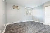Located at 511 W Doty St in Madison, WI, this efficient one-bedroom, one-bathroom unit offers a well-organized layout across a single floor. The main living area is generously sized relative to the overall footprint, featuring durable wood-look laminate flooring, neutral gray walls, and a textured ceiling throughout. A ceiling fan with light fixture provides both air circulation and overhead lighting, while a wall-mounted air conditioning unit and baseboard heating ensure year-round comfort. A window along the exterior wall allows natural light to filter into the space and offers a view of the surrounding greenery outside.

The kitchen area is seamlessly integrated into the main living space and is equipped with white cabinetry, a white electric range, a refrigerator, and a sink with countertop workspace. Upper cabinets provide practical storage, and under-cabinet lighting adds functional illumination to the cooking area.

The bedroom includes a sliding door closet with a hanging rod, offering straightforward storage solutions. The bathroom is accessed via a warm-toned wood door and features a combined tub and shower unit, a toilet, and a vanity, all finished in clean white tones with matching wood-look flooring that ties the space together cohesively.