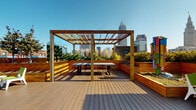 Located at 725 Johnson Ct in Cleveland's vibrant Ohio City neighborhood, this exceptional rooftop terrace offers an elevated outdoor experience with breathtaking, panoramic views of the downtown Cleveland skyline, including the iconic Terminal Tower. The space is thoughtfully designed with rich composite wood decking that runs throughout, providing a warm and durable foundation for the entire rooftop.

A central pergola constructed from natural wood serves as a focal point, providing partial shade over an outdoor dining area equipped with a table and chairs — ideal for gatherings or al fresco dining. Flanking the main walkway are generously sized raised garden beds crafted from warm-toned cedar planking, filled with a lush variety of ornamental grasses, flowering plants, shrubs, and trees that add vibrant greenery and seasonal color to the urban setting.

A second pergola-style archway frames the entrance to the space, accented by blooming purple flowers that add a pop of color. Gravel areas between plantings enhance the natural aesthetic while minimizing maintenance. The rooftop is fully accessible via a dedicated entry door and is equipped with safety features including a fire extinguisher. Under open skies, the combination of abundant plantings, thoughtful architectural elements, and sweeping city views makes this rooftop terrace a truly remarkable urban outdoor retreat.