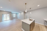 This well-appointed 2-bedroom, 2-bathroom unit at 12 Station St in Middleborough, MA offers a thoughtfully designed single-floor layout with a clean, modern aesthetic throughout. The open-concept kitchen and living area serves as the heart of the home, featuring light hardwood flooring, recessed lighting, and sliding glass doors that fill the space with natural light and provide access to an outdoor balcony overlooking a well-maintained lawn. The kitchen is equipped with gray shaker-style cabinetry, stainless steel appliances, a large center island with a white quartz countertop, an integrated sink, and pendant lighting — ideal for both everyday cooking and entertaining. The spacious primary bedroom offers generous proportions, soft carpeting, and multiple windows with views of the surrounding greenery, complemented by a walk-in closet with built-in wire shelving. The second bedroom is similarly carpeted with natural light from a window. Both bathrooms are finished in a modern style, with one featuring a gray vanity with white countertop, tile flooring, and a glass-enclosed shower. Two closets provide ample storage throughout. The building exterior showcases a classic combination of gray siding and brick, with a neatly landscaped setting in a residential Middleborough neighborhood.