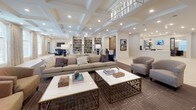 Located at 2470 Merchant Street in Frederick, Maryland, this single-floor community clubhouse offers an expansive and elegantly designed gathering space that blends comfort with refined style. The welcoming lobby greets visitors with light-toned hardwood flooring, shiplap-clad walls, bold black double entry doors, and a reception desk — all illuminated by recessed lighting for a bright, airy atmosphere.

The main lounge area is a standout, featuring soaring coffered ceilings with detailed millwork, generous arched windows that fill the room with natural light, and a curated arrangement of neutral sofas, accent chairs, and marble-topped coffee tables set atop a richly patterned area rug. A full built-in bookcase serves as an architectural focal point, adding warmth and character to the space.

A dedicated dining and media nook offers built-in bench seating, navy blue upholstered chairs, dining tables, and a wall-mounted flat-screen TV flanked by shiplap detailing and sconce lighting — ideal for social gatherings or casual viewing.

A game and activity area provides additional versatility, showcasing a large game table, navy seating, and a curated gallery wall featuring vibrant large-format artwork above white cabinetry. Throughout the space, the design palette of warm neutrals, navy accents, and gold-toned hardware creates a cohesive, upscale ambiance suited for community connection.