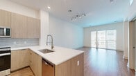 Located at 40 William St in Wellesley Hills, MA, this thoughtfully designed one-bedroom, two-bathroom residence offers a clean, contemporary aesthetic throughout. The open-concept kitchen and living area serves as the heart of the home, featuring warm hardwood flooring, recessed lighting, and large sliding glass doors that invite abundant natural light into the living room. The kitchen is outfitted with flat-front cabinetry in a light wood finish, a tile backsplash, stainless steel appliances including a side-by-side refrigerator and range, and a central island with a white quartz countertop and built-in sink — ideal for both cooking and casual dining. A hallway finished with large-format marble-look porcelain tile connects the main living spaces to the private quarters. The bedroom is carpeted for comfort, features a generous window with exterior views, and includes access to a dedicated closet as well as built-in shelving — a practical touch for storage and organization. Both bathrooms continue the marble-tile aesthetic, with one featuring a full soaking tub and tiled surround. The overall palette of crisp whites and natural wood tones creates a bright, cohesive, and welcoming atmosphere throughout.
