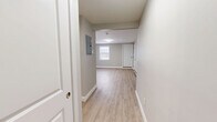 Located at 144 Dunbarton Rd in Manchester, New Hampshire, this efficiently designed single-floor unit offers a thoughtful layout comprising a living room, kitchen area, hallway, and a full bathroom. Throughout the space, light wood-look luxury vinyl flooring creates a clean, cohesive aesthetic that complements the neutral gray and white color palette on the walls and trim.

The open living area is bright and functional, featuring a window that allows natural light to filter in, white panel doors, and baseboard heating. An electrical panel is conveniently accessible from the hallway entry.

The kitchen is well-appointed with crisp white shaker-style cabinetry, stainless steel appliances including a refrigerator, electric range, and over-the-range microwave, as well as a single-basin sink. The layout makes efficient use of the available space while maintaining a modern, clean appearance.

The bathroom is finished with a full soaking tub and shower combination unit with built-in shelving, complemented by brushed gold fixtures that add a warm, contemporary touch. The light flooring and white walls keep the space feeling fresh and open.

Overall, the unit presents a move-in-ready, modern interior with consistent finishes, practical amenities, and a straightforward layout well-suited for comfortable everyday living.