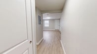 Located at 144 Dunbarton Rd in Manchester, New Hampshire, this efficiently designed single-floor unit offers a thoughtful layout comprising a living room, kitchen area, hallway, and a full bathroom. Throughout the space, light wood-look luxury vinyl flooring creates a clean, cohesive aesthetic that complements the neutral gray and white color palette on the walls and trim.

The open living area is bright and functional, featuring a window that allows natural light to filter in, white panel doors, and baseboard heating. An electrical panel is conveniently accessible from the hallway entry.

The kitchen is well-appointed with crisp white shaker-style cabinetry, stainless steel appliances including a refrigerator, electric range, and over-the-range microwave, as well as a single-basin sink. The layout makes efficient use of the available space while maintaining a modern, clean appearance.

The bathroom is finished with a full soaking tub and shower combination unit with built-in shelving, complemented by brushed gold fixtures that add a warm, contemporary touch. The light flooring and white walls keep the space feeling fresh and open.

Overall, the unit presents a move-in-ready, modern interior with consistent finishes, practical amenities, and a straightforward layout well-suited for comfortable everyday living.