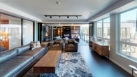 Located at 1500 Commerce St in downtown Tacoma, Washington, this single-floor space combines contemporary design with versatile functionality. The open-concept interior is anchored by a spacious lounge area furnished with rich leather sofas and armchairs arranged around a solid wood coffee table atop a textured area rug. Track lighting runs throughout the ceiling, providing adjustable illumination across the entire floor.

Glass-paneled sliding partitions divide portions of the interior, offering flexible configurations for private gatherings or open-flow events. A built-in media wall with a fireplace serves as a focal point in the main lounge area, adding warmth and visual interest.

The fully equipped kitchen features a large central island with bar seating, matte stone countertops, stainless steel appliances including double wall ovens and a gas range, a ventilation hood, and contemporary cabinetry. Dramatic pendant lighting above the island completes the professional-grade aesthetic.

The space opens directly onto a generous outdoor terrace with modern seating and panoramic views of the Tacoma skyline and Commencement Bay waterfront. The seamless indoor-outdoor connection, combined with the clean architectural lines and upscale finishes throughout, creates a polished and inviting environment well-suited for professional or social gatherings.