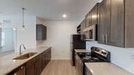 This single-story residence offers a thoughtfully designed layout with a clean, contemporary aesthetic throughout. The kitchen serves as a functional centerpiece, featuring rich dark espresso-toned shaker-style cabinetry paired with granite-look countertops, a subway tile backsplash, and a full suite of stainless steel appliances including a refrigerator, electric range, and over-the-range microwave. Light wood-tone luxury vinyl plank flooring runs through the kitchen and connects to the main living areas, lending warmth and continuity.

The living area is generously proportioned, finished with plush neutral-toned carpeting, a ceiling fan with light fixture, and French doors that invite natural light and provide outdoor access. The bedrooms are similarly carpeted, with one featuring a window overlooking greenery and a ceiling fan for added comfort.

The bathrooms reflect the same refined finishes found throughout the home. One bathroom includes a dark vanity with a granite-topped sink and a glass-enclosed walk-in shower, while another offers a full tub-shower combination with chrome fixtures. Light wood-tone flooring extends through both bathrooms, tying the overall design together for a cohesive and polished living environment.