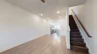 This two-story home in Warner Robins, Georgia, offers a clean, contemporary design defined by crisp white walls, light wood-tone flooring, and recessed lighting throughout. The main level features an open living area that flows directly into the kitchen, creating a cohesive and functional layout. A ceiling fan overhead and recessed lighting provide comfortable illumination, while the open sightlines between rooms enhance the sense of spaciousness.

The kitchen is a standout feature, equipped with gray shaker-style cabinetry, white countertops, and a full suite of stainless steel appliances including a range, microwave, dishwasher, and refrigerator. A central island with pendant lighting above adds both prep space and visual interest. Natural light enters through multiple windows that offer views of the surrounding neighborhood. A convenient half bathroom is also located on the main level.

The staircase, finished with dark wood treads and a clean railing, leads to the upper floor, where the bedrooms are situated. The primary bedroom features large windows, a ceiling fan, a walk-in closet, and darker wood-tone flooring. A full bathroom with a tub-shower combination, vanity, and wood-look flooring serves the upper level. The overall ambiance is bright, modern, and move-in ready.