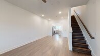 This two-story home in Warner Robins, Georgia, offers a clean, contemporary design defined by crisp white walls, light wood-tone flooring, and recessed lighting throughout. The main level features an open living area that flows directly into the kitchen, creating a cohesive and functional layout. A ceiling fan overhead and recessed lighting provide comfortable illumination, while the open sightlines between rooms enhance the sense of spaciousness.

The kitchen is a standout feature, equipped with gray shaker-style cabinetry, white countertops, and a full suite of stainless steel appliances including a range, microwave, dishwasher, and refrigerator. A central island with pendant lighting above adds both prep space and visual interest. Natural light enters through multiple windows that offer views of the surrounding neighborhood. A convenient half bathroom is also located on the main level.

The staircase, finished with dark wood treads and a clean railing, leads to the upper floor, where the bedrooms are situated. The primary bedroom features large windows, a ceiling fan, a walk-in closet, and darker wood-tone flooring. A full bathroom with a tub-shower combination, vanity, and wood-look flooring serves the upper level. The overall ambiance is bright, modern, and move-in ready.