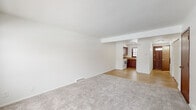 This two-floor residence offers a practical and well-organized layout with consistent finishes throughout. The main living area is spacious and open, featuring plush wall-to-wall carpeting and a neutral white color palette that creates a bright, clean atmosphere. A textured ceiling adds subtle character to the living space, which flows seamlessly into the kitchen through a defined passageway. The kitchen is equipped with rich dark-toned cabinetry, laminate countertops, and white appliances including a range and dishwasher. A window above the sink allows natural light to fill the space, and light hardwood-style flooring ties the kitchen and adjacent areas together. Multiple bedrooms are found throughout the home, each carpeted and featuring multi-pane windows with dark wood trim that invite natural light and views of the outdoors. Closet storage is available in select bedrooms. The bathroom is clean and functional, featuring a tub-shower combination, a single-sink vanity with a mirrored medicine cabinet, and bright overhead lighting. A staircase connects the two floors, and baseboard heating vents are present throughout, ensuring year-round comfort. The overall design is understated and move-in ready.