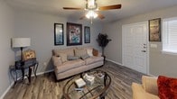 This single-floor home offers a thoughtfully designed layout that balances comfort and functionality across its key living spaces. Throughout the residence, wood-look flooring in a weathered gray tone provides a cohesive and modern aesthetic.

The living room serves as a welcoming gathering space, featuring a ceiling fan with light, a tiled fireplace, and a window fitted with blinds that allows natural light to filter in. The room comfortably accommodates a seating area and provides a relaxed, neutral ambiance.

The kitchen is equipped with white cabinetry offering ample storage, granite-style countertops, a double basin sink, and a black dishwasher. Its clean, bright design makes it both practical and visually appealing.

The primary bedroom includes a ceiling fan, a window with blinds for natural light, and closet access, creating a cozy and private retreat. A secondary bedroom mirrors this layout with its own ceiling fan and window, offering flexible use as a guest room or home office.

Both bathrooms are finished with granite-style vanity countertops, white cabinetry, tub-shower combinations with tile surrounds, and the same wood-look flooring found throughout the home. The result is a consistent, clean, and modern finish that ties the entire space together.