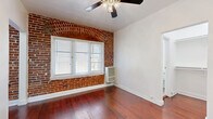 Located at 1616 North Normandie Avenue in the heart of Los Angeles, this single-floor unit offers a well-organized layout comprising a living room, kitchen, bathroom, and hallway. Rich, warm hardwood flooring runs throughout the main living areas, lending a classic character to the space.

The living room is a bright and open area anchored by a striking exposed brick accent wall featuring an arched window detail — a standout architectural element that adds historic charm. Natural light filters in through white-shuttered windows, and a ceiling fan provides comfortable airflow.

The kitchen is efficiently designed with dark espresso-stained wood cabinetry, granite-style countertops, and stainless steel appliances including a gas range and full-size refrigerator. The rich cabinetry contrasts beautifully with the warm hardwood floors that continue into this space.

The bathroom offers a clean, all-white aesthetic with tile flooring, a full soaking tub with overhead shower, a classic pedestal sink, and a mirrored medicine cabinet. Dual windows allow natural light to brighten the room.

The hallway connects the spaces efficiently, contributing to the unit's practical flow. Overall, this unit blends vintage architectural details — most notably the exposed brick and hardwood floors — with functional modern fixtures throughout.