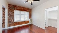 Located at 1616 North Normandie Avenue in the heart of Los Angeles, this single-floor unit offers a well-organized layout comprising a living room, kitchen, bathroom, and hallway. Rich, warm hardwood flooring runs throughout the main living areas, lending a classic character to the space.

The living room is a bright and open area anchored by a striking exposed brick accent wall featuring an arched window detail — a standout architectural element that adds historic charm. Natural light filters in through white-shuttered windows, and a ceiling fan provides comfortable airflow.

The kitchen is efficiently designed with dark espresso-stained wood cabinetry, granite-style countertops, and stainless steel appliances including a gas range and full-size refrigerator. The rich cabinetry contrasts beautifully with the warm hardwood floors that continue into this space.

The bathroom offers a clean, all-white aesthetic with tile flooring, a full soaking tub with overhead shower, a classic pedestal sink, and a mirrored medicine cabinet. Dual windows allow natural light to brighten the room.

The hallway connects the spaces efficiently, contributing to the unit's practical flow. Overall, this unit blends vintage architectural details — most notably the exposed brick and hardwood floors — with functional modern fixtures throughout.