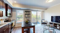Located in the heart of Saint Paul, this single-floor communal amenity space offers a refined blend of modern design and warm, inviting finishes. The interior lounge is anchored by rich hardwood flooring and striking exposed wooden ceiling beams that lend a sense of architectural character throughout. A fully equipped kitchenette lines one wall, featuring dark wood cabinetry, white quartz countertops, a beverage refrigerator, a sink, and a geometric patterned tile backsplash — all framed by a wall-mounted flat-screen TV overhead. Elegant pendant lighting illuminates a central island with seating, creating a natural gathering point for socializing. Wainscoting in a muted sage-green palette adds a sophisticated, layered look to the walls. A windowed nook area with high-top tables and bar stools offers views of the surrounding cityscape, while French doors open to a spacious rooftop terrace. The outdoor deck is thoughtfully appointed with Adirondack chairs surrounding a fire pit, an outdoor dining table, a gas grill, and an exterior television — all set against panoramic views of downtown Saint Paul. This versatile space is ideal for hosting events or relaxing in an upscale urban setting.