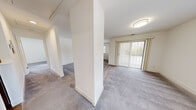Located at 30 Greenview Circle in West Sayville, NY, this single-floor residence offers a clean, move-in-ready layout designed for comfortable everyday living. The main living area is generously proportioned, featuring soft grey carpeting and a distinctive structural column that adds architectural character while subtly defining separate zones within the open space. Large vertical-blind-covered sliding glass doors and multiple windows flood the area with natural light and provide views of the surrounding neighborhood. The space flows seamlessly from one area to the next, creating an open and airy ambiance throughout. A dedicated entryway with a paneled door leads to a stairwell accessing a lower level, adding convenient storage or utility potential. The kitchen is thoughtfully appointed with crisp white shaker-style cabinetry, grey countertops, stainless steel appliances, and warm wood-look flooring — a bright and functional workspace. Notably, an in-unit stacked washer and dryer is tucked neatly within the kitchen corridor, offering exceptional convenience. The carpeted bedrooms are well-sized, each featuring windows with blinds that allow for natural light and neighborhood views. Throughout the unit, white walls and consistent finishes create a cohesive, neutral palette ready for personalization.