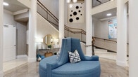 Located at 510 N Wilmington Street in Raleigh, NC, this well-appointed amenity floor offers a refined blend of architectural grandeur and functional design across a generously sized single-level layout. The centerpiece is a dramatic two-story lobby characterized by soaring ceilings, tall white columns, and a sweeping dual staircase with elegant iron railings. A circular blue upholstered lounge seat anchors the space beneath a cascading cluster pendant chandelier, while herringbone-patterned tile flooring adds visual texture underfoot. A wall-mounted elevator provides convenient vertical access, and large windows at the far end of the hallways flood the space with natural light and views of the outdoor courtyard. The conference room offers an intimate meeting setting, featuring a round wood-top table surrounded by mid-century-style chairs, a wall-mounted television, bold chevron-patterned wallcovering, and a sculptural overhead light fixture. The game room presents a more relaxed atmosphere, with light hardwood flooring, a sleek billiards table, multiple wall-mounted televisions, comfortable lounge seating, and direct access to the outdoor area through floor-to-ceiling glass doors. A large historical photographic mural adds a locally inspired character to the space. Connecting hallways with recessed lighting and curated artwork tie each area together seamlessly.