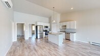 Located at 535 Hickory Street in Wrightstown, Wisconsin, this well-appointed single-floor home offers three bedrooms and two bathrooms within a thoughtfully designed layout. The open-concept kitchen and living area serves as the heart of the home, anchored by soaring vaulted ceilings that lend an airy, expansive feel. The kitchen is outfitted with crisp white shaker cabinetry, granite countertops, a central island with pendant lighting, and a full suite of stainless steel appliances including a refrigerator, range, microwave, and dishwasher. Light wood-look flooring flows consistently throughout the entire space, creating a clean and cohesive aesthetic. The living room is highlighted by a striking corner fireplace with a white surround and large sliding glass doors that frame serene waterfront views, flooding the space with natural light. Both bathrooms continue the granite countertop theme with white vanity cabinetry, and one features a full tub-shower combination. The bedrooms are bright and comfortably sized, with the generous primary bedroom offering ample space. A dedicated closet rounds out the layout. Neutral tones and modern finishes give this home a fresh, move-in-ready appeal throughout.