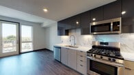 This single-floor unit showcases a thoughtfully designed contemporary interior with a cohesive aesthetic carried throughout each space. The kitchen serves as a standout feature, combining dark, high-gloss upper cabinetry with light wood-toned lower cabinets for a striking two-tone contrast. A marble-look backsplash runs the full length of the counters, complementing the clean white quartz countertops. Stainless steel appliances — including a gas range, built-in microwave, dishwasher, and French door refrigerator — complete the well-equipped cooking space. Wood-look flooring flows consistently through the kitchen and into the open living area, enhancing the sense of continuity.

The bedrooms are bright and neutral, each featuring wood-look flooring, clean white walls, and windows that bring in natural light and offer views of the surrounding cityscape. Dark-framed doors add a bold, modern accent against the lighter palette.

The bathroom maintains the same contemporary sensibility, featuring light wood cabinetry, a white quartz vanity top, an oversized backlit mirror, and wood-look tile flooring. A soaking tub and walk-in shower with tiled surround complete the well-appointed space, delivering both style and function.