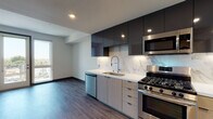 This single-floor unit showcases a thoughtfully designed contemporary interior with a cohesive aesthetic carried throughout each space. The kitchen serves as a standout feature, combining dark, high-gloss upper cabinetry with light wood-toned lower cabinets for a striking two-tone contrast. A marble-look backsplash runs the full length of the counters, complementing the clean white quartz countertops. Stainless steel appliances — including a gas range, built-in microwave, dishwasher, and French door refrigerator — complete the well-equipped cooking space. Wood-look flooring flows consistently through the kitchen and into the open living area, enhancing the sense of continuity.

The bedrooms are bright and neutral, each featuring wood-look flooring, clean white walls, and windows that bring in natural light and offer views of the surrounding cityscape. Dark-framed doors add a bold, modern accent against the lighter palette.

The bathroom maintains the same contemporary sensibility, featuring light wood cabinetry, a white quartz vanity top, an oversized backlit mirror, and wood-look tile flooring. A soaking tub and walk-in shower with tiled surround complete the well-appointed space, delivering both style and function.
