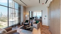 Located on South Michigan Avenue in Chicago's vibrant Grant Park corridor, this elevated amenity floor delivers a striking combination of contemporary design and breathtaking vistas. Floor-to-ceiling curtain-wall windows flood the open-plan layout with abundant natural light while framing sweeping panoramic views of Lake Michigan to the east and the iconic Chicago skyline to the north and west.

Rich herringbone-patterned hardwood flooring flows seamlessly throughout the space, anchoring the refined aesthetic. The main lounge area centers around a substantial wood coffee table and plush seating arrangements, all beneath dramatic cascading pendant light fixtures that add warmth and visual depth to the high ceilings. Recessed cove lighting further enhances the sophisticated ambiance.

A dedicated conference or private dining area features a large marble-topped table surrounded by upholstered seating, set directly against full-height glazing with unobstructed city views—an ideal setting for formal gatherings. Thoughtfully designed nook seating along one wall provides intimate spaces for smaller groups or individual use.

Large sliding barn-style doors in a warm wood tone allow flexible division of the space, while neutral tones of grey, taupe, and cream are punctuated by emerald green accent pieces throughout. The overall design is polished, modern, and tailored for both social and professional use.