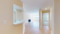 This single-floor residence is thoughtfully laid out with a clear separation between living, sleeping, and functional spaces. The main living area features light hardwood-style flooring and a white tile-surround fireplace as a central focal point, flanked by large windows fitted with horizontal blinds that allow generous natural light to fill the room. The open layout connects seamlessly to a dining or secondary living space, which flows into a peninsula kitchen equipped with light wood cabinetry, white countertops, a stainless steel undermount sink, and a full suite of stainless steel appliances including a gas range, over-the-range microwave, and refrigerator.

The bedrooms are finished with plush neutral carpeting and feature windows that bring in natural light; one bedroom includes sliding glass door access to an outdoor space with tree-lined views. Additional carpeted rooms offer versatile use and ample wall space. The bathroom is fitted with a wood-toned vanity, white countertop, a large mirror, and modern strip lighting above. Throughout the residence, warm beige tones, white trim, and consistent finishes create a cohesive and calm ambiance.