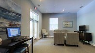 Located at 3590 Mary Adele Ave in Charleston, SC, this single-story space presents a clean, professional atmosphere well-suited for client-facing or office use. The interior is finished in soft gray tones throughout, creating a calm and inviting environment. Elevated ceilings with recessed lighting add a sense of openness to the space, while large transom windows and standard windows along the exterior walls allow generous amounts of natural light to filter in, offering views of the surrounding greenery outside.

The main area features neutral carpeting underfoot and is furnished with striped upholstered armchairs arranged around a central seating area, alongside a dark wood desk or reception counter near the entrance — suggesting a waiting or reception function. Wall art with coastal-inspired hues complements the subdued color palette. The layout is open and uncluttered, lending the space a sense of ease and accessibility. Overall, the design balances practicality with a welcoming aesthetic, reflecting a thoughtfully arranged professional environment in the Charleston area.