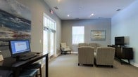 Located at 3590 Mary Adele Ave in Charleston, SC, this single-story space presents a clean, professional atmosphere well-suited for client-facing or office use. The interior is finished in soft gray tones throughout, creating a calm and inviting environment. Elevated ceilings with recessed lighting add a sense of openness to the space, while large transom windows and standard windows along the exterior walls allow generous amounts of natural light to filter in, offering views of the surrounding greenery outside.

The main area features neutral carpeting underfoot and is furnished with striped upholstered armchairs arranged around a central seating area, alongside a dark wood desk or reception counter near the entrance — suggesting a waiting or reception function. Wall art with coastal-inspired hues complements the subdued color palette. The layout is open and uncluttered, lending the space a sense of ease and accessibility. Overall, the design balances practicality with a welcoming aesthetic, reflecting a thoughtfully arranged professional environment in the Charleston area.