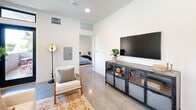 Located at 2450 S Barrington Ave in Los Angeles, CA, this thoughtfully designed one-bedroom, one-bathroom unit offers a efficient and modern living experience across a single floor. The open-plan kitchen and living area serves as the heart of the home, featuring polished concrete floors, recessed lighting, and a bright, airy ambiance. The kitchen is well-appointed with stainless steel appliances including a full-size refrigerator, electric range, and built-in microwave, complemented by light wood cabinetry, open shelving, dark countertops, and a tiled backsplash. A stacked in-unit washer and dryer adds everyday convenience. The living area provides a comfortable retreat with large windows framing lush tree views, flooding the space with natural light. The bedroom is a serene and well-proportioned room featuring soft carpeting, a large window overlooking greenery, and vaulted ceiling details that enhance the sense of space. A dedicated walk-in closet with built-in shelving and hanging rods offers ample storage. The bathroom is finished with floor-to-ceiling vertical subway tile surrounding a soaking tub and shower combination enclosed by a glass panel, delivering a clean, spa-like aesthetic. Overall, the unit presents a cohesive modern design throughout.