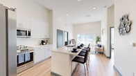 Located at 7000 Kiran Patel Dr in Winter Garden, Florida, this two-bedroom, three-bathroom residence offers a thoughtfully designed open-concept layout with impressively high ceilings that amplify the sense of space throughout. Light-toned hardwood flooring flows seamlessly from the kitchen through the living area, enhancing the bright, airy atmosphere.

The kitchen is a standout feature, boasting white shaker cabinetry reaching to the ceiling, a herringbone tile backsplash, quartz countertops, and a full suite of stainless steel appliances. A spacious island with bar seating provides both additional prep space and a casual dining area. The adjacent living room benefits from abundant natural light pouring through full-height sliding glass doors that open to an outdoor area.

The primary bedroom is a generously proportioned retreat with soaring ceilings, hardwood flooring, and direct access to a private en-suite bathroom featuring a glass-enclosed walk-in shower and a dedicated walk-in closet with built-in shelving. The second bedroom offers large windows with bright outdoor views and wood flooring. Two additional bathrooms serve the residence, one featuring a full soaking tub with tile surround. Signature teal door frames throughout add a modern, distinctive design accent to this well-appointed Winter Garden home.