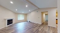 This single-story home is defined by its vaulted ceiling in the main living area, accented by exposed beams and recessed lighting that create a bright, open atmosphere. The living room is generously proportioned, featuring warm hardwood-style flooring, neutral beige walls, and a classic fireplace with a white mantel as a focal point. A large window allows natural light to fill the space while offering views of surrounding greenery.

The kitchen is equipped with warm oak cabinetry, dark granite countertops, a stainless steel gas range, built-in microwave, and a single-basin sink — offering a practical and well-appointed cooking space. Hardwood-style flooring continues throughout the kitchen and main areas.

A hallway connects the living spaces to the bedrooms, which feature plush carpeting, ceiling fans, and windows providing natural light. The bathroom includes a tub-shower combination, white cabinetry with dark countertops, and hardwood-style flooring. An in-unit washer and dryer are conveniently tucked behind bifold doors near the bathroom. Additional flexible living space with recessed lighting and hardwood-style flooring rounds out the home's layout.