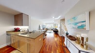 Located at 230 First Ave in Boston's Charlestown neighborhood, this well-designed three-bedroom, three-bathroom residence offers a thoughtful layout across a single floor. The open-concept living and dining area serves as the heart of the home, showcasing rich hardwood flooring that flows seamlessly throughout. Large windows flood the living space with natural light and provide views of the surrounding neighborhood, creating a bright and welcoming atmosphere. The kitchen features granite countertops, warm wood cabinetry, and a functional island with seating, connecting effortlessly to the dining and living areas. The primary bedroom is a comfortable retreat with plush carpeting, dual windows, and a serene, neutral palette. The two additional bedrooms are equally well-appointed with soft carpeting and tasteful finishes, each offering ample closet space. The three bathrooms are clean and modern — one features large-format travertine tile surrounding a soaking tub and a separate glass shower, while another offers classic white subway tile with a tub-shower combination. Warm beige tones and stone-topped vanities complete the bathrooms' refined look. A hallway and dedicated closet round out the efficient and comfortable floor plan of this Boston residence.