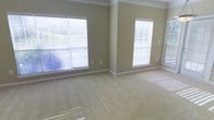 This single-floor space presents a spacious, open room finished with wall-to-wall plush carpeting in a warm neutral tone, creating a comfortable and inviting atmosphere. The walls are painted in a soft beige, contributing to the overall light and airy feel of the interior. Crown molding runs along the ceiling perimeter, adding a refined architectural detail that elevates the room's character. Multiple large windows fitted with white horizontal blinds line two walls, allowing abundant natural light to filter throughout the space and casting bright, even illumination across the room. The windows also offer the flexibility to control light and privacy as needed. White baseboards provide clean contrast against the neutral walls and flooring, lending a crisp, well-maintained appearance. The open layout offers considerable flexibility for furniture arrangement and use of space. The overall ambiance is calm and understated, with a clean, move-in-ready condition that serves as a blank canvas for personalization.