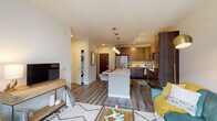 This well-appointed single-floor residence features a thoughtfully designed open-concept layout that seamlessly connects the kitchen, dining, and living areas. The kitchen is a standout feature, showcasing rich two-tone cabinetry in warm walnut and dark espresso finishes, a full suite of stainless steel appliances including a refrigerator, range, and microwave, a subway tile backsplash, and a central island with a light quartz countertop that doubles as a dining bar with seating. Pendant lighting and track lighting illuminate the space effectively. Wood-look plank flooring runs throughout the main living areas, adding warmth and continuity.

The living area is generously proportioned and opens directly to a private balcony through a full-width sliding glass door, allowing natural light to flow in and providing outdoor views of the surrounding community. A dedicated in-unit laundry closet with a stacked washer and dryer is conveniently located near the main living space.

The bedroom is comfortably sized with plush carpeting, a ceiling fan, large windows that bring in natural light, and a spacious walk-in closet with built-in shelving. The bathroom features a sliding-door walk-in shower, light wood-look tile flooring, and clean, neutral finishes throughout.