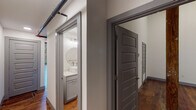 Located at 601 S Fifth St in Easley, South Carolina, this two-floor loft showcases a striking blend of historic industrial character and contemporary updates. The main living level immediately impresses with original hardwood floors exhibiting rich tonal variation, soaring wood-beam ceilings, and dramatic exposed brick walls punctuated by large arched windows that flood the space with natural light and frame outdoor greenery. Pendant lighting and a steel-and-wood staircase add refined industrial accents that complement the raw architectural bones.

The kitchen is outfitted with sleek gray cabinetry, marble-veined quartz countertops, and stainless steel appliances including a range and over-the-range microwave — a polished counterpoint to the loft's heritage aesthetic. Bathrooms throughout are well-appointed with gray vanities, round mirrors, and clean white fixtures, with one featuring tile flooring and another continuing the hardwood motif.

The upper level offers additional rooms with ceiling fans, including one with warm carpeting beneath an exposed wood ceiling with industrial pipe accents, and another with original hardwood floors. Throughout both floors, five-panel gray doors and exposed ductwork reinforce the cohesive industrial-modern design language, creating a dynamic and characterful living environment.