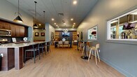 Located at 6741 W 135th St in Overland Park, Kansas, this single-floor amenity center offers a generous and thoughtfully designed space for recreation, fitness, and socializing. The layout encompasses a modern fitness center, a versatile social lounge, a game room, and a fully equipped kitchen area.

The fitness center is a standout feature, boasting high ceilings with an exposed industrial-style roof structure, ceiling fans, and expansive floor-to-ceiling windows that flood the space with natural light and outdoor views. It is outfitted with a comprehensive array of equipment including treadmills, ellipticals, strength machines, free weights, exercise balls, and a dedicated stretching and functional training area with rubberized flooring and wall mirrors.

The social lounge presents a warm, inviting atmosphere with soft blue-gray walls, luxury vinyl plank flooring, and eclectic contemporary décor including curated artwork. Flexible seating arrangements include lounge sofas, dining tables, and high-top bar seating, all centered around a wall-mounted television and decorative stacked wood feature wall. A full kitchen with dark wood cabinetry, granite countertops, and bar stools supports entertaining and gatherings.

A dedicated game room features a pool table, shuffleboard, and billiard-themed wall art. A carpeted corridor with dual handrails and art displays connects the various areas of this well-rounded community facility.